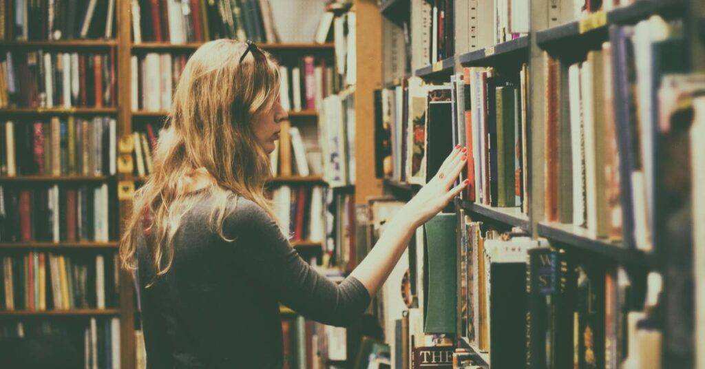 Person browsing bookshelves in a cozy library, symbolizing curiosity and discovery for book lovers.