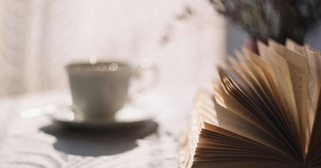 An open book placed beside a cup of tea in soft sunlight, capturing a calm and cozy reading moment.