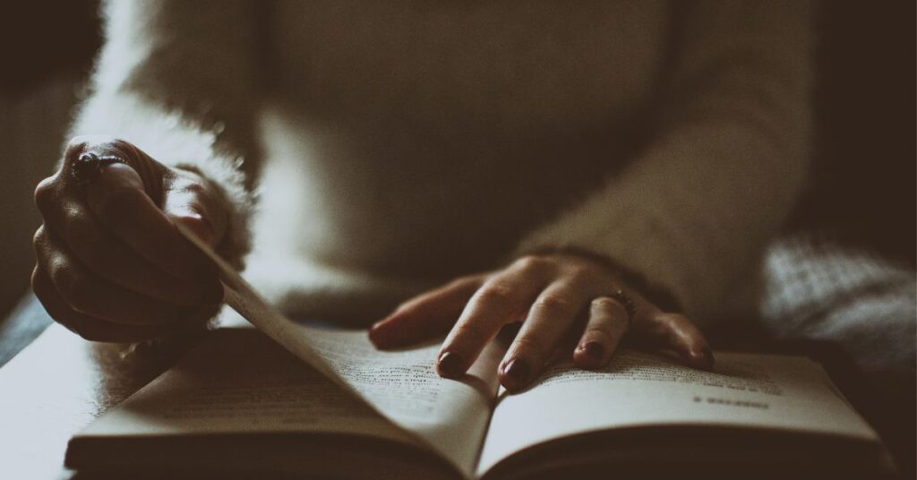 Hands turning pages of a book in soft shadowed light, capturing the dark academia mood of The Secret History by Donna Tartt.